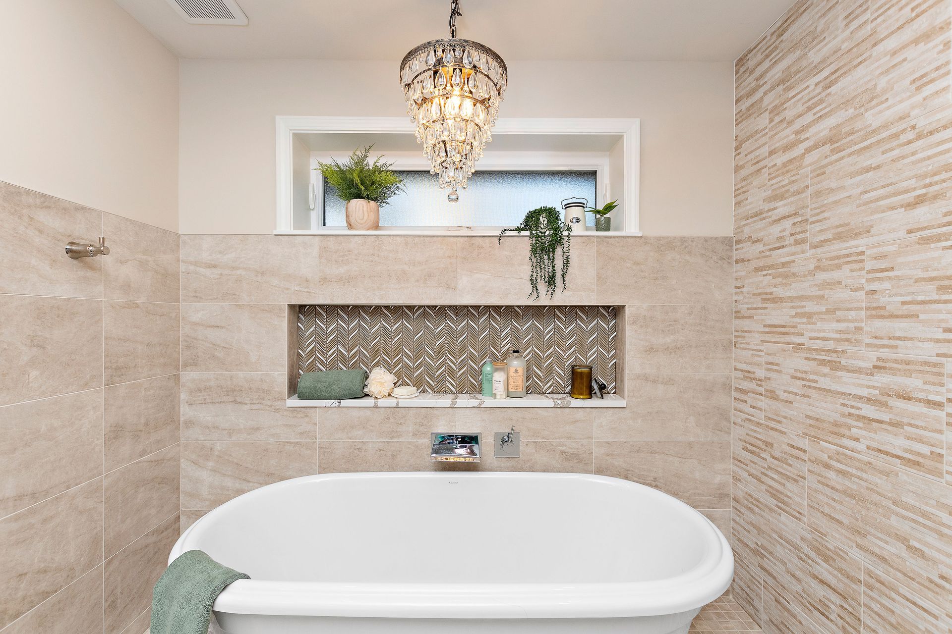 There is a bathtub in the bathroom with a chandelier hanging from the ceiling.