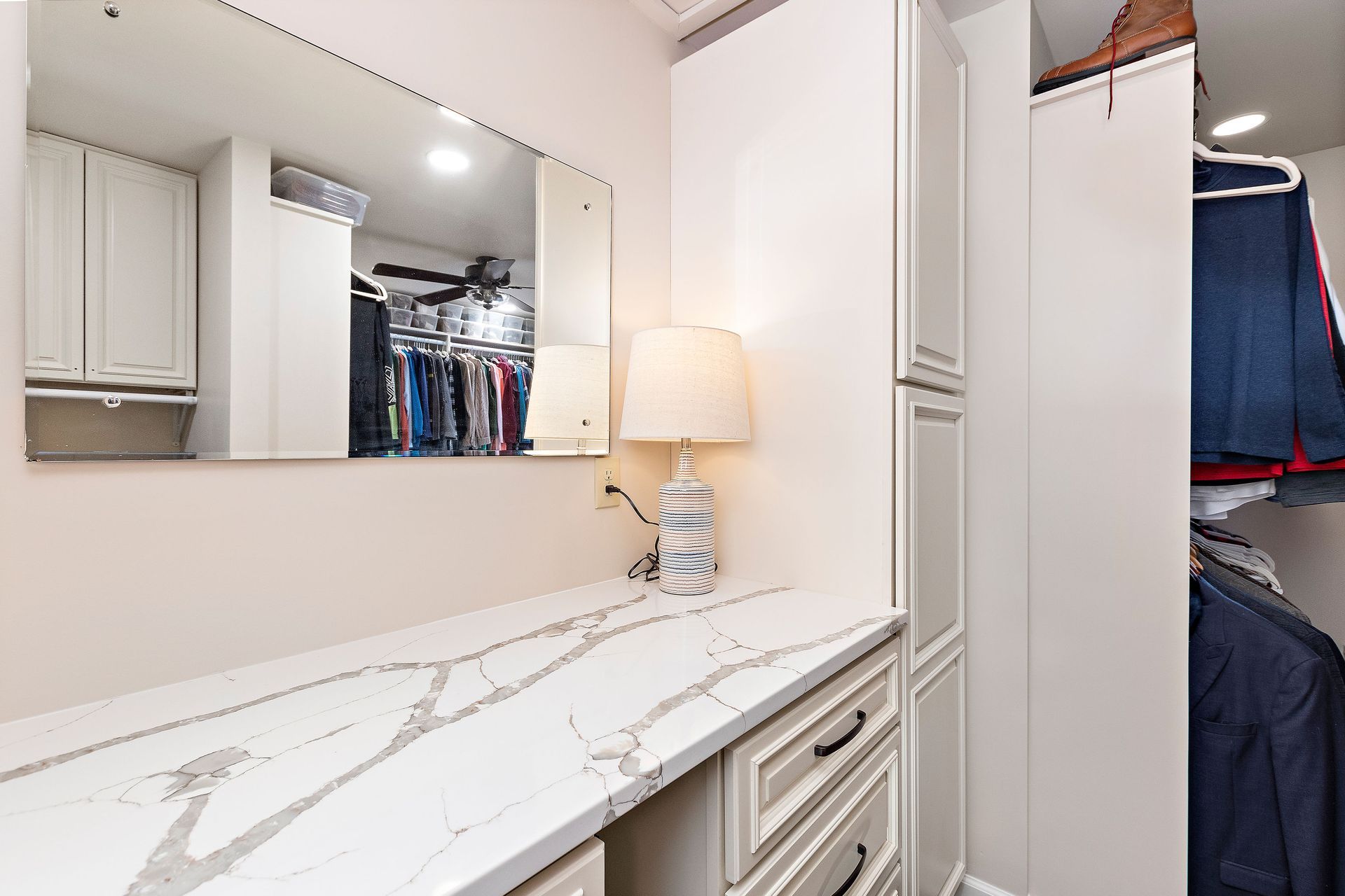 A walk in closet with a desk , mirror and lamp.