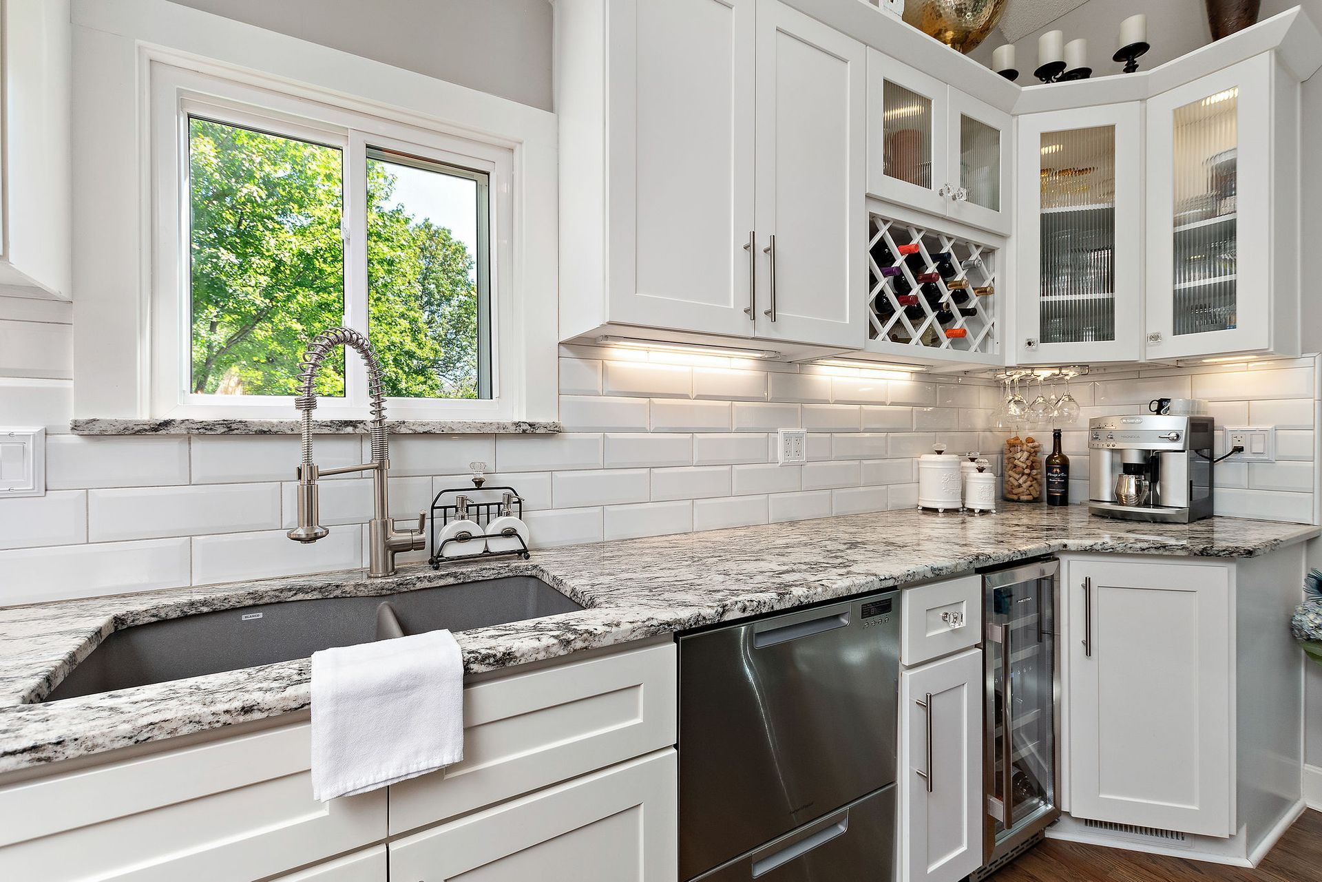 A kitchen with white cabinets , granite counter tops , stainless steel appliances and a window.