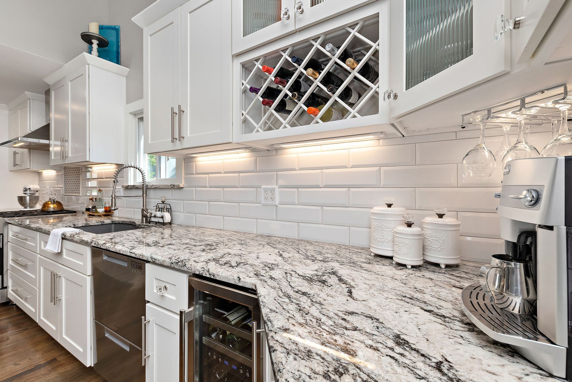 A kitchen with granite counter tops , white cabinets , stainless steel appliances and a wine rack.