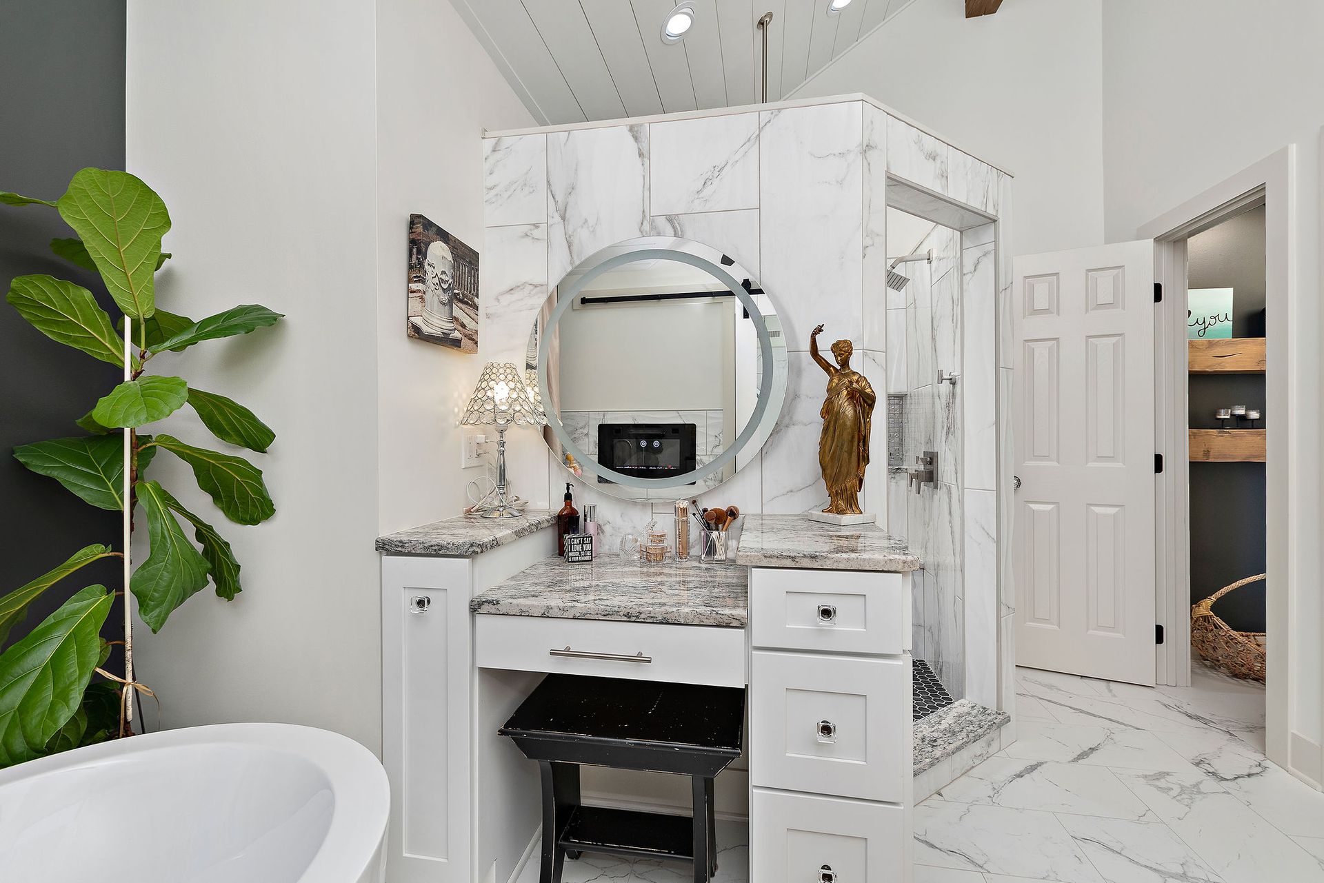 A bathroom with a tub , vanity , mirror and statue.