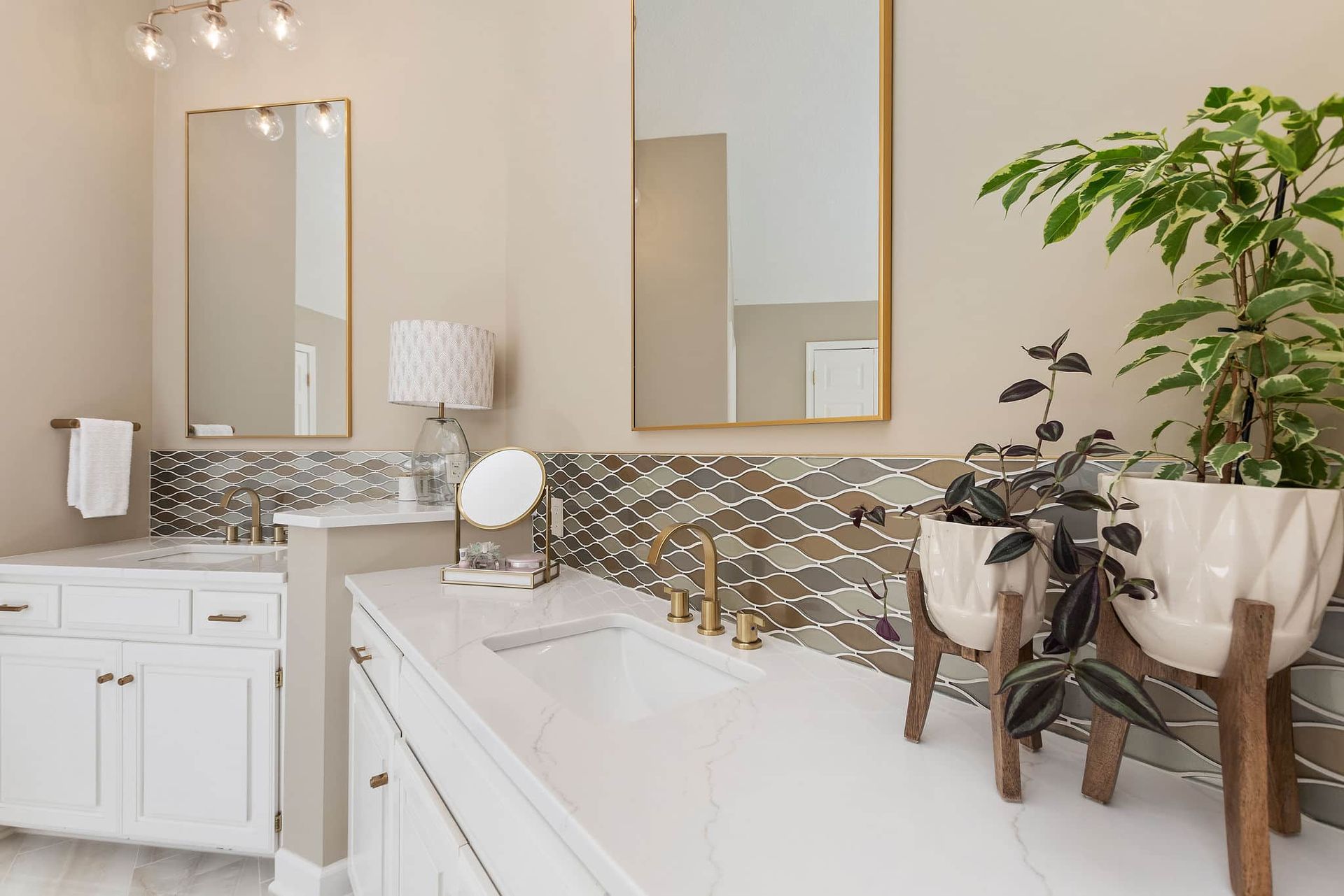 A bathroom with two sinks , two mirrors and a plant.