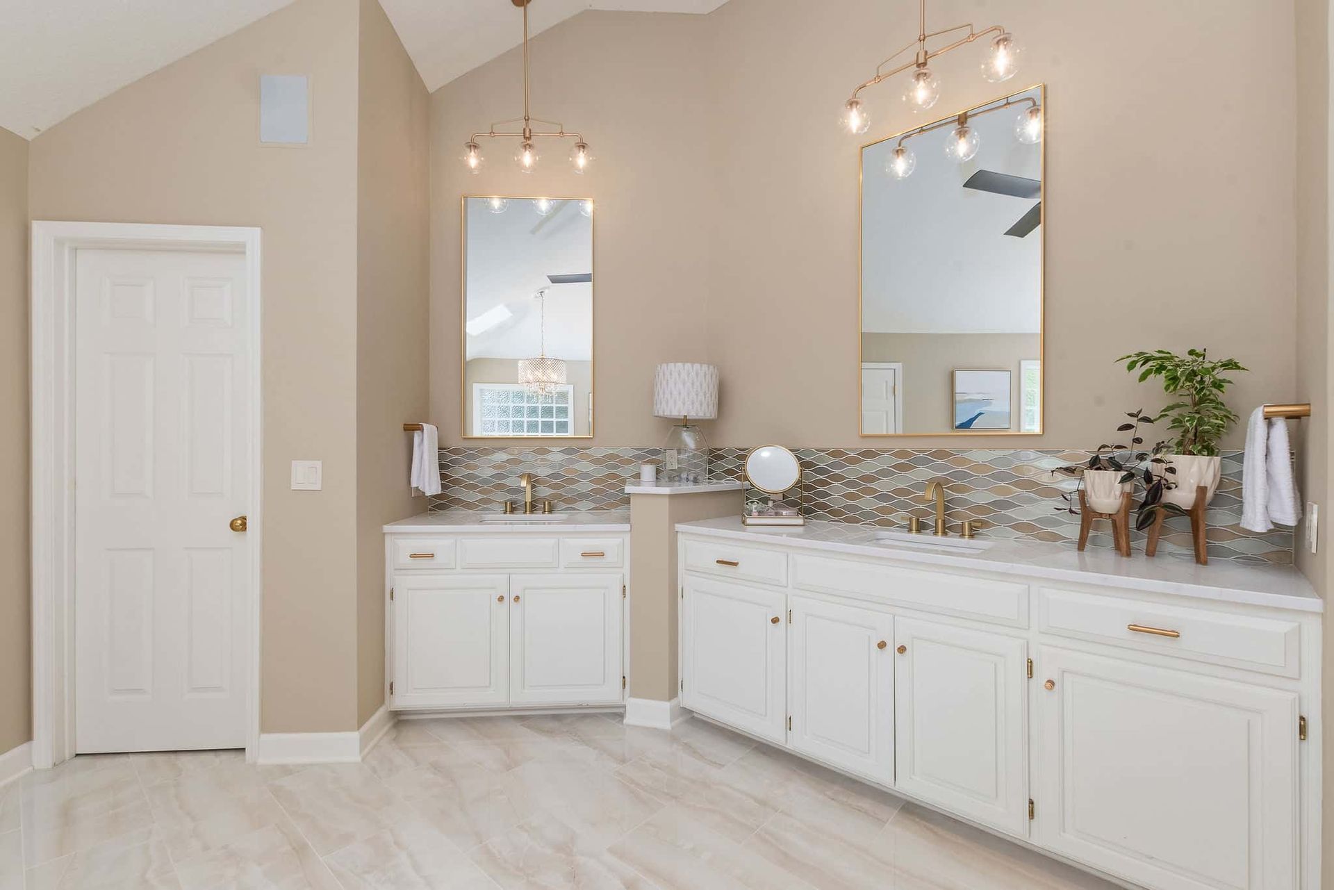 A bathroom with two sinks , a mirror , and white cabinets.