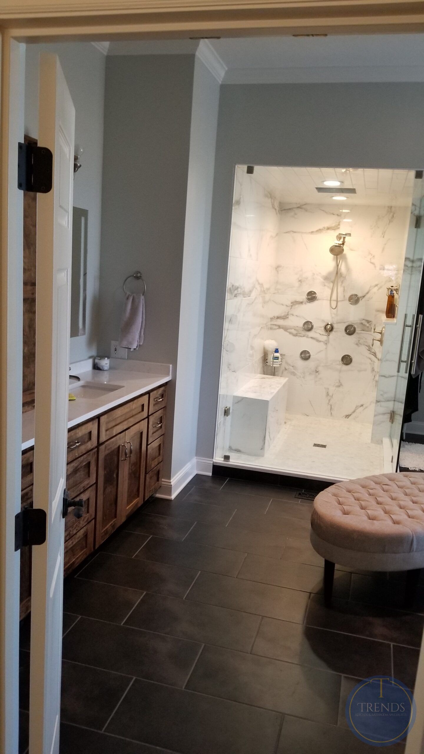 A bathroom with a walk in shower , sink , and ottoman.