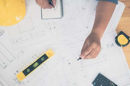 A person is sitting at a table drawing on a blueprint.