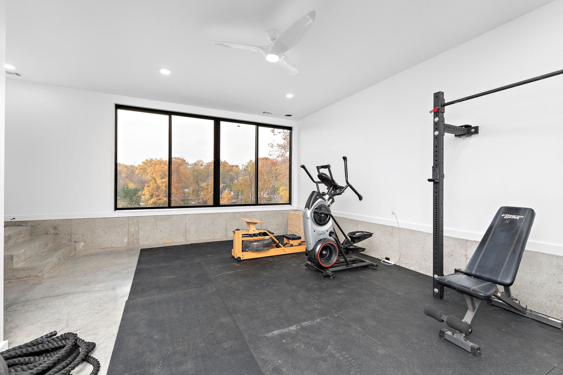There is a gym in the garage with a lot of windows and exercise equipment.