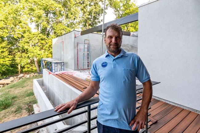 A man in a blue shirt is standing on a balcony next to a building under construction.