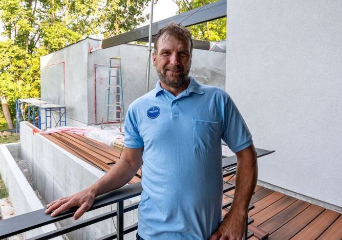 A man in a blue shirt is standing on a balcony next to a building under construction.