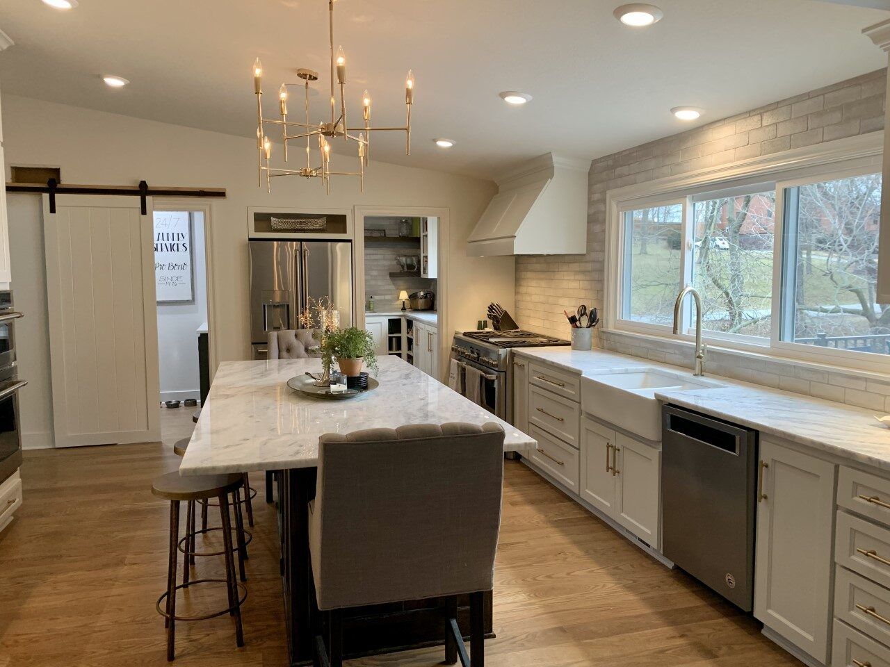 A kitchen with white cabinets , stainless steel appliances , a large island and a chandelier.