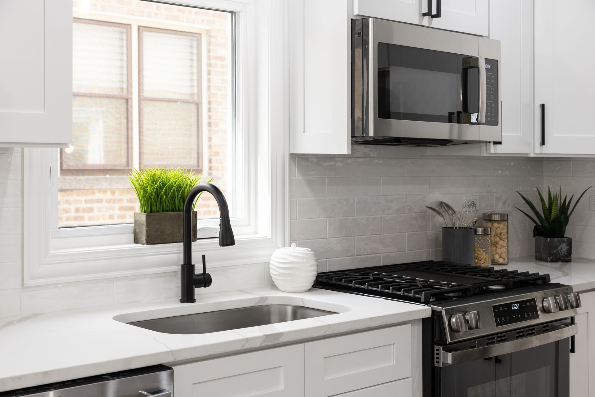A kitchen with a sink , stove , microwave and window.