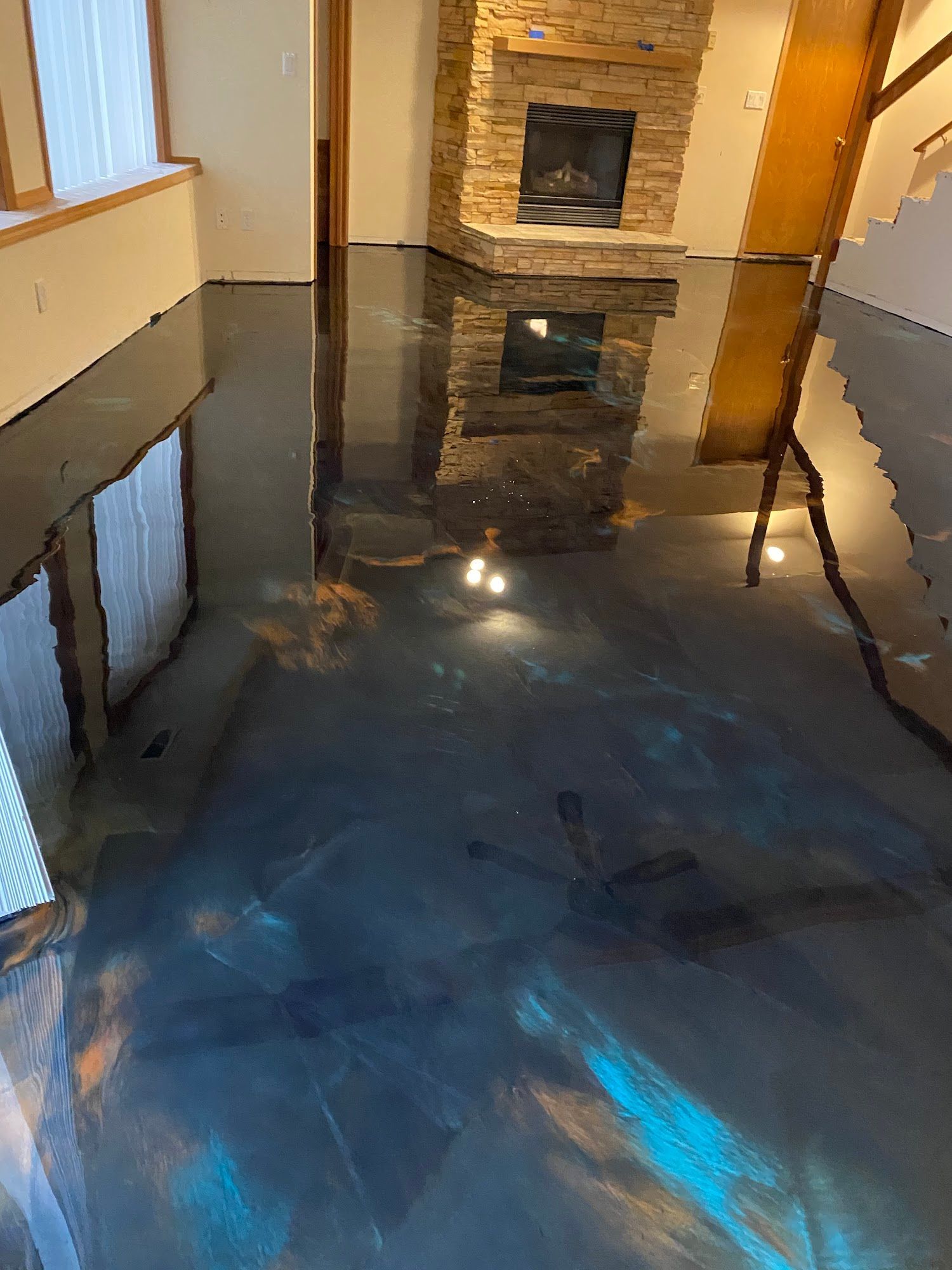 Shiny epoxy floor with blue, gold, and bronze swirls reflects fireplace and interior.