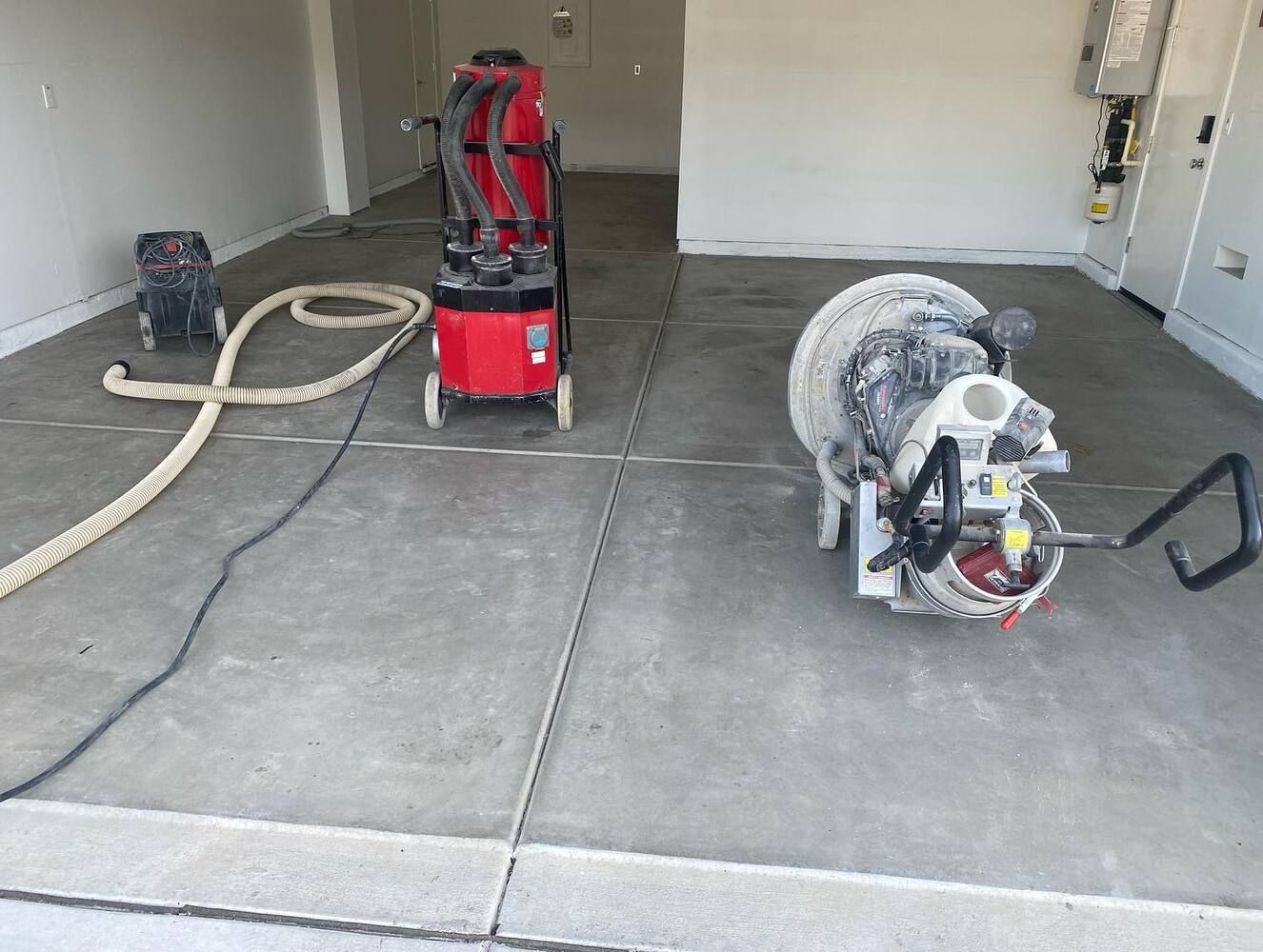 Concrete floor grinding equipment in a garage; red vacuum and grinding machine.