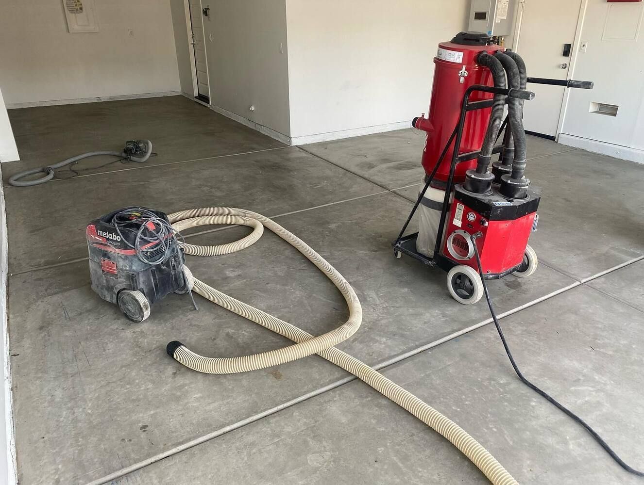 Concrete floor grinding equipment in a room, with vacuum and hose.