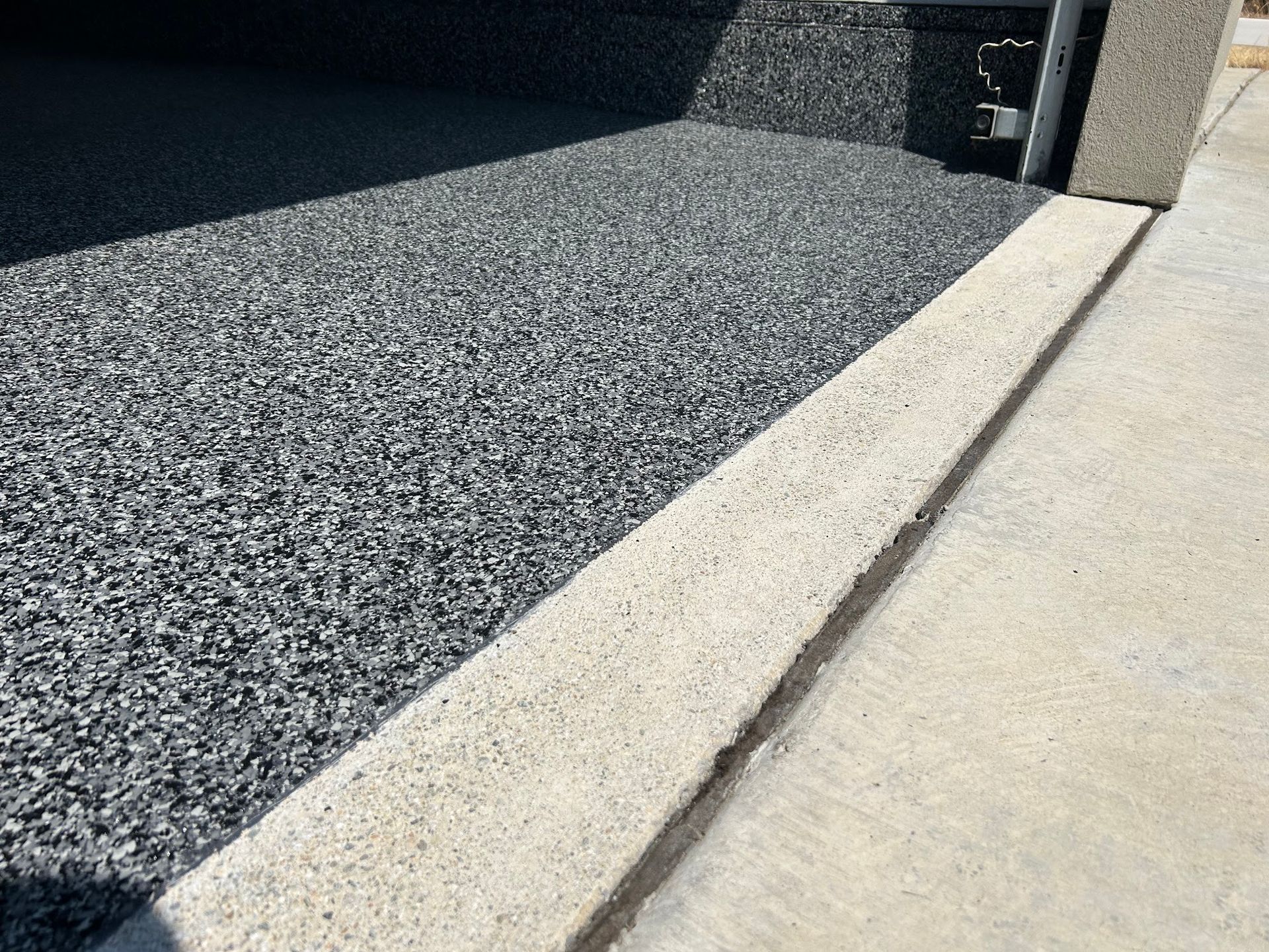 Dark speckled flooring next to a light concrete sidewalk and border, leading into a garage.