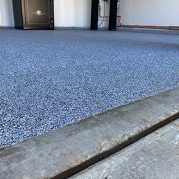 Close-up of a garage floor with a blue speckled epoxy finish. A concrete edge is in the foreground.