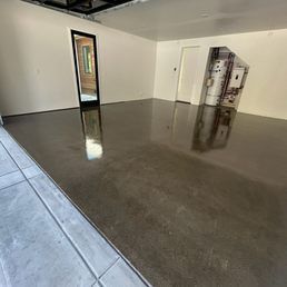 Newly coated concrete floor reflecting a bright light, inside an empty room with white walls and a doorway.