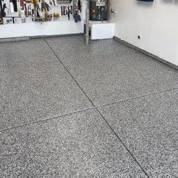 Garage floor with speckled gray epoxy coating, visible joint lines. Tools on wall.