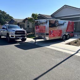 A truck pulling a trailer with company advertisement parked in front of a house.
