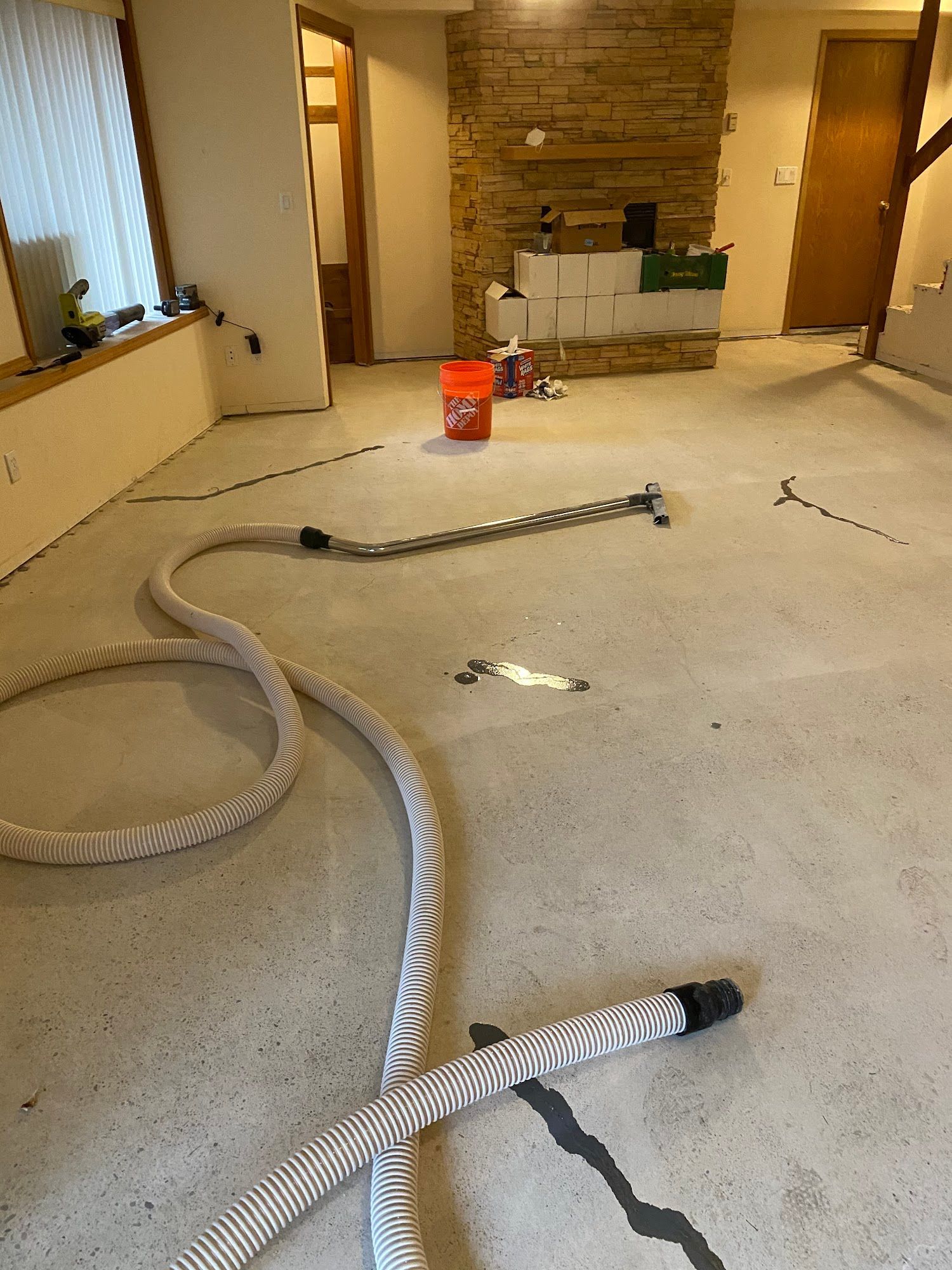 Hoses and tools on a concrete floor in a room under construction, with a fireplace in the background.