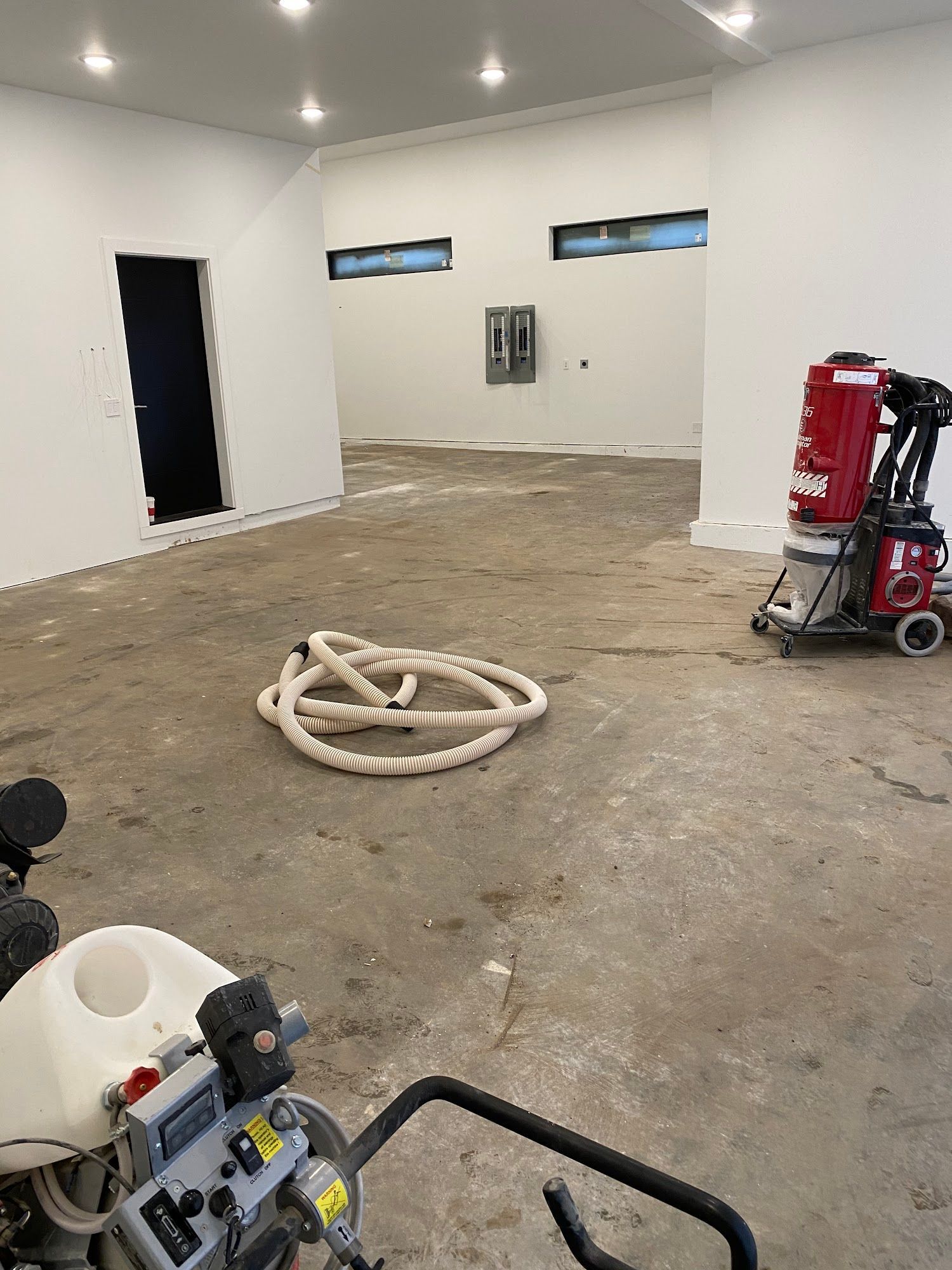 Construction site interior with white walls, exposed concrete floor, and equipment.