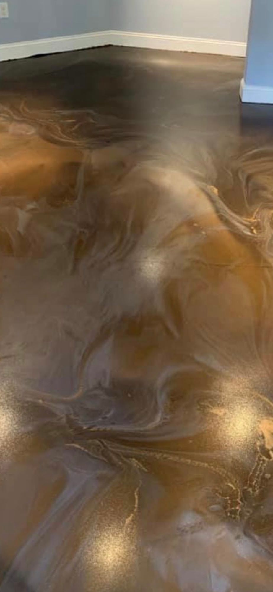 Metallic epoxy flooring with swirling brown and white tones, reflecting light.