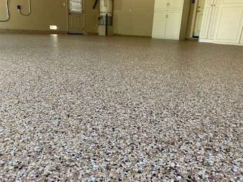 Epoxy-coated garage floor with multi-colored chips; beige, white, and black flecks. Cabinets and door in background.