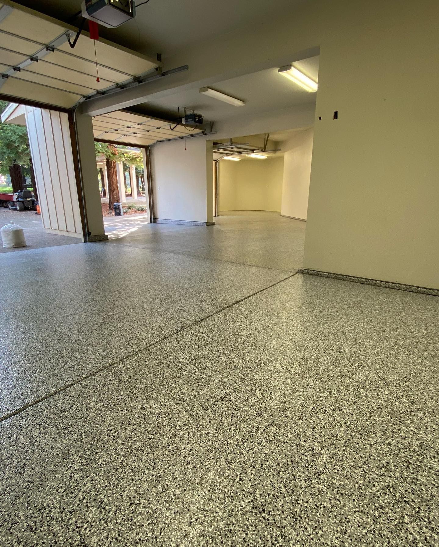 Garage with epoxy-coated floor. Garage door open. Neutral walls, fluorescent lighting.