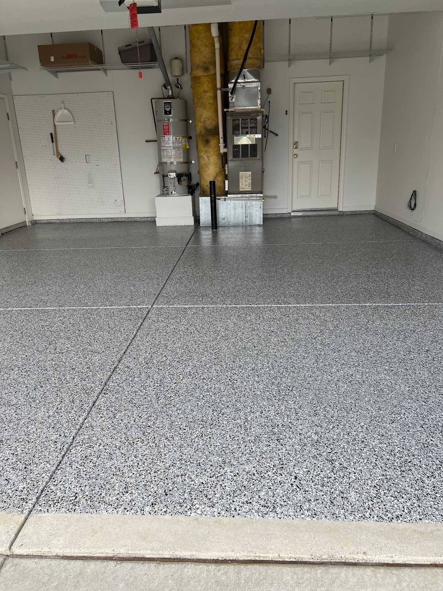 A garage with a gray speckled epoxy floor, utility installations, and a white door.