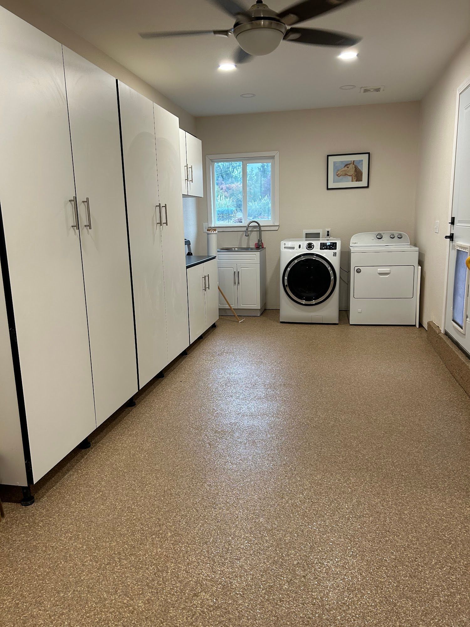 Laundry room with white cabinets, washer, dryer, sink, and speckled tan floor.