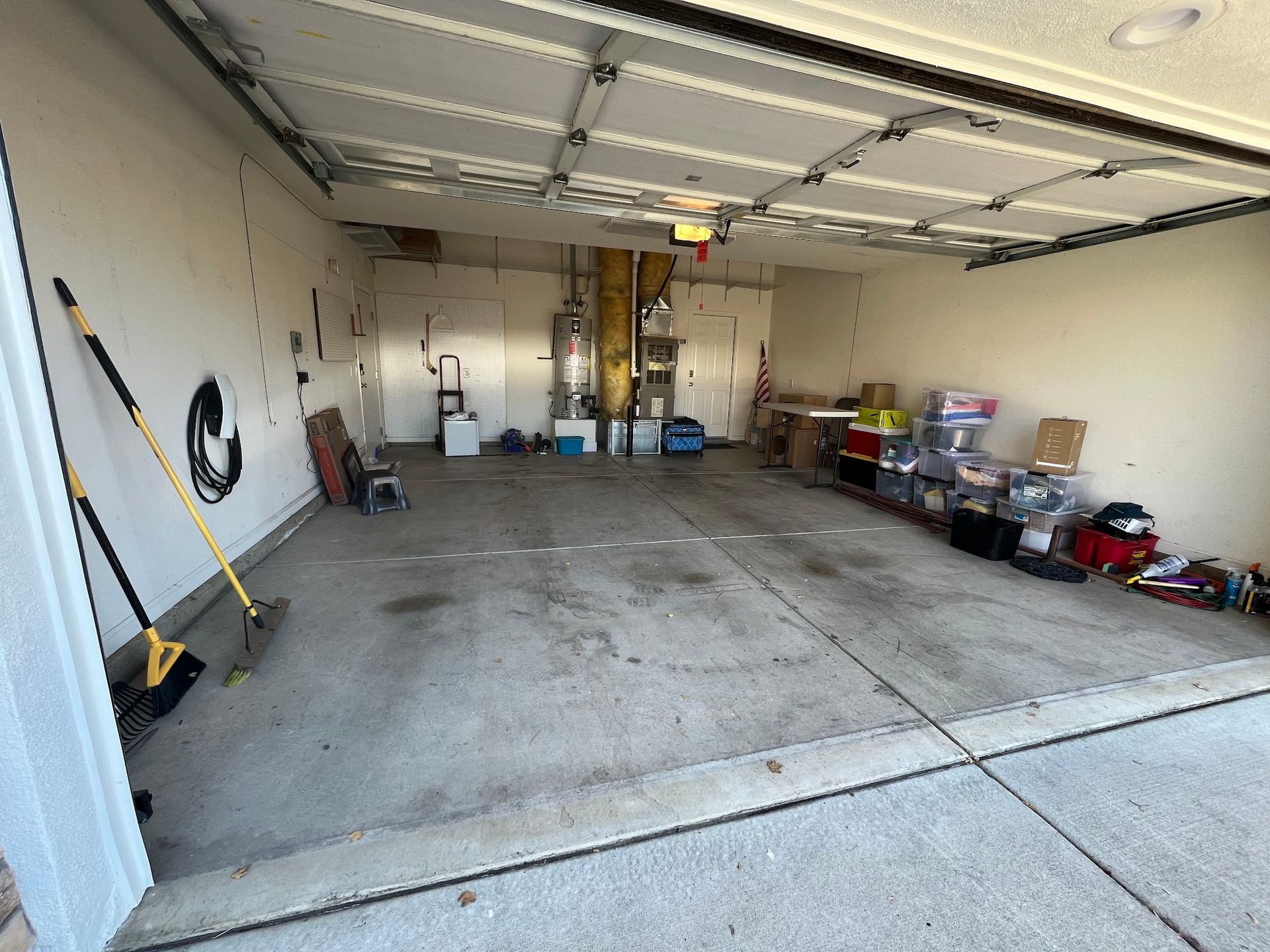 Empty garage with concrete floor, cluttered shelves, water heater, and a closed garage door.
