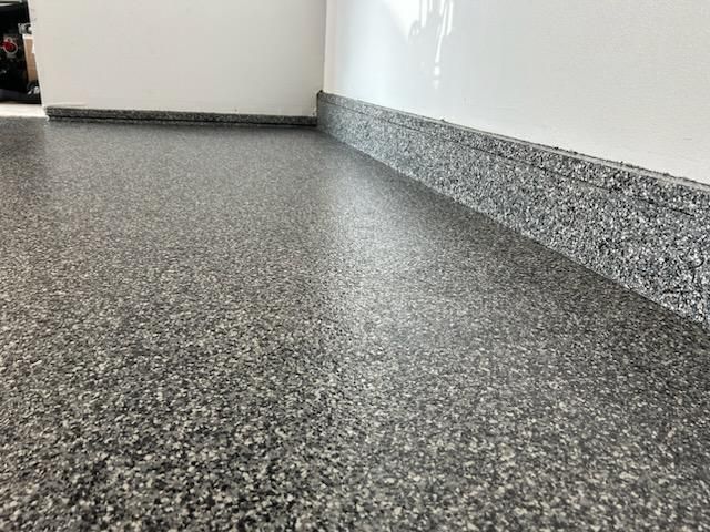 Gray speckled epoxy garage floor with a matching baseboard against a white wall.