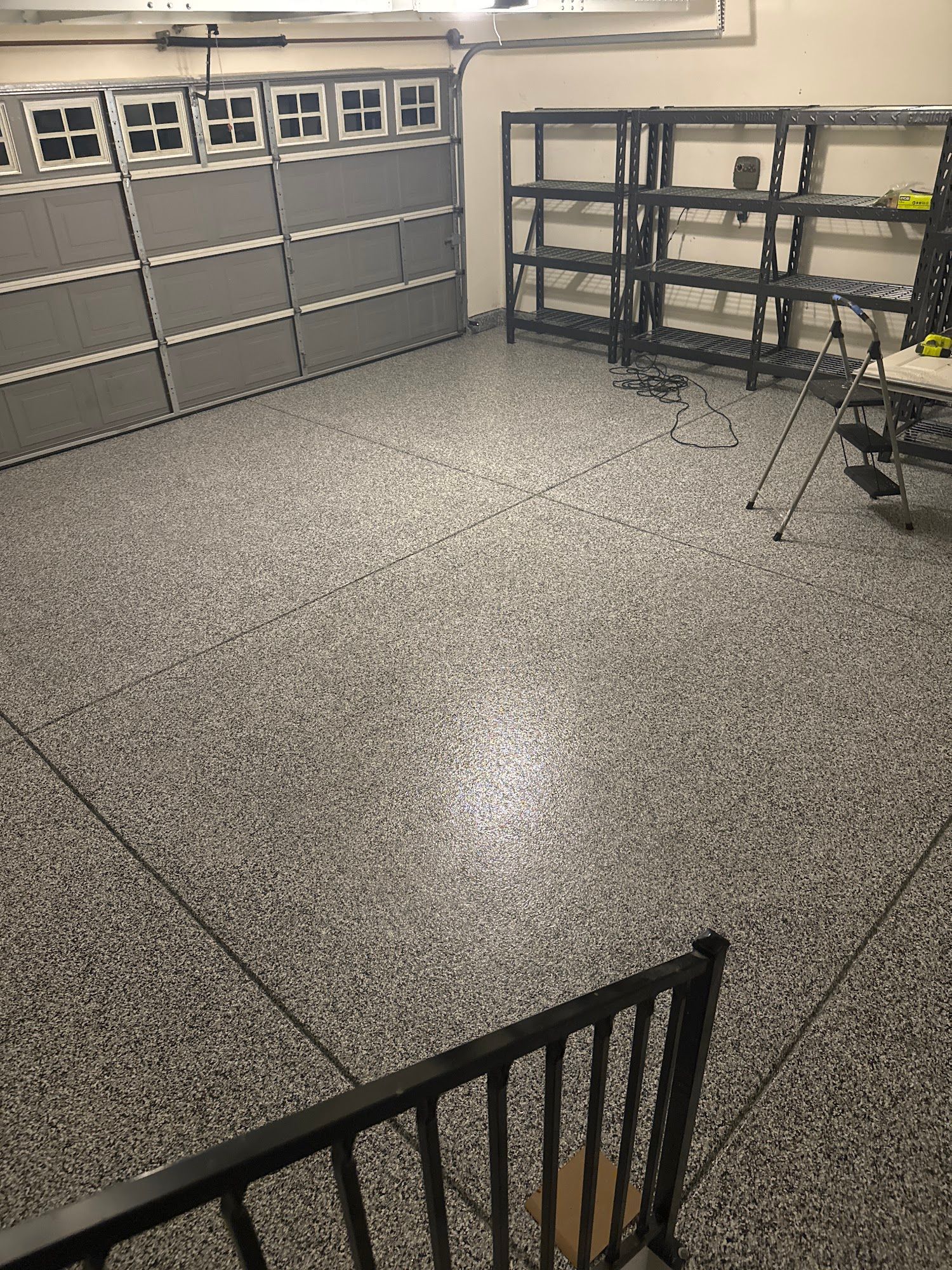 Garage interior with gray speckled floor, garage door, metal shelving, and a railing.