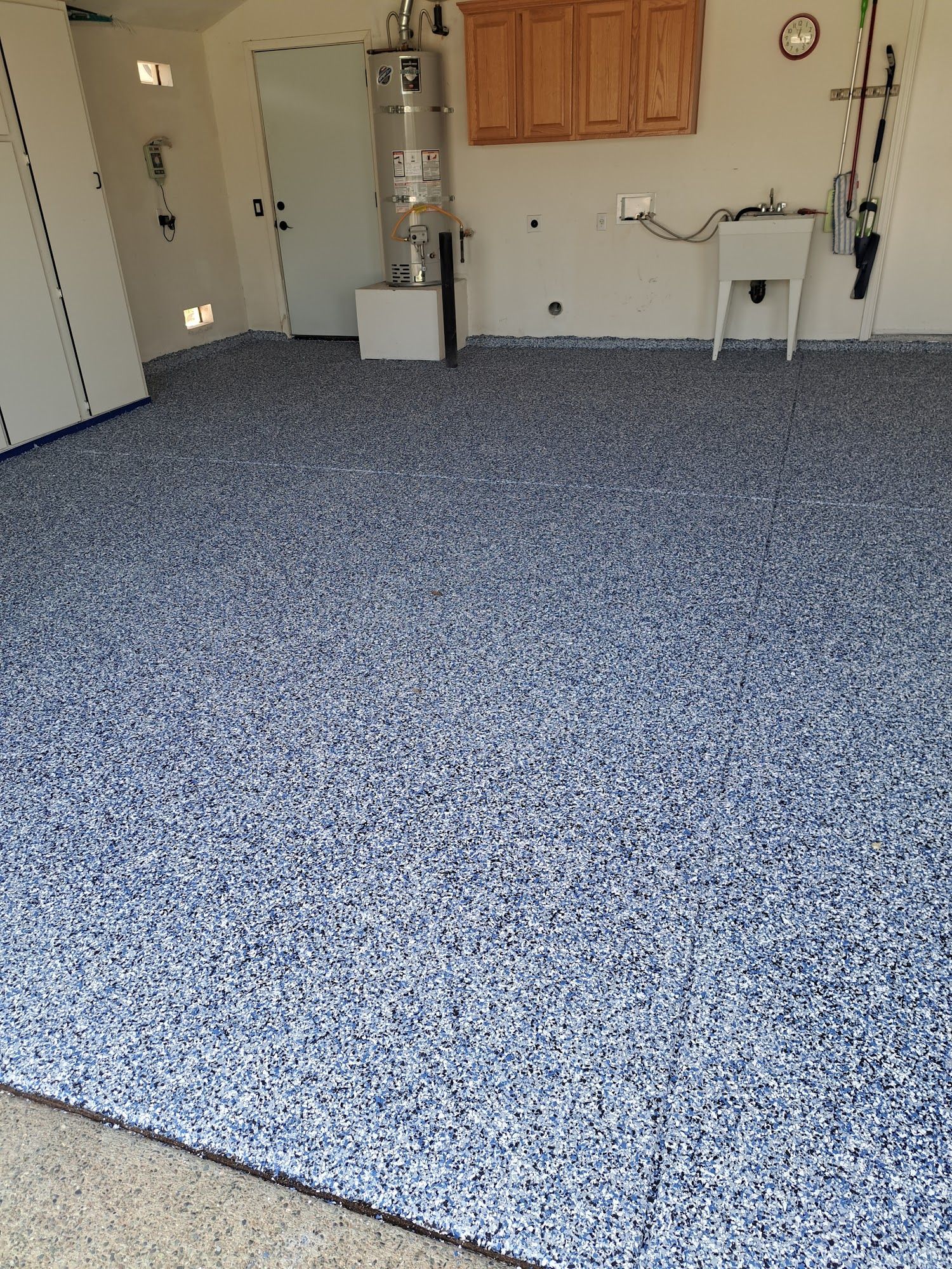 Garage with a blue and white speckled epoxy floor. Cabinets, sink, and water heater are visible.