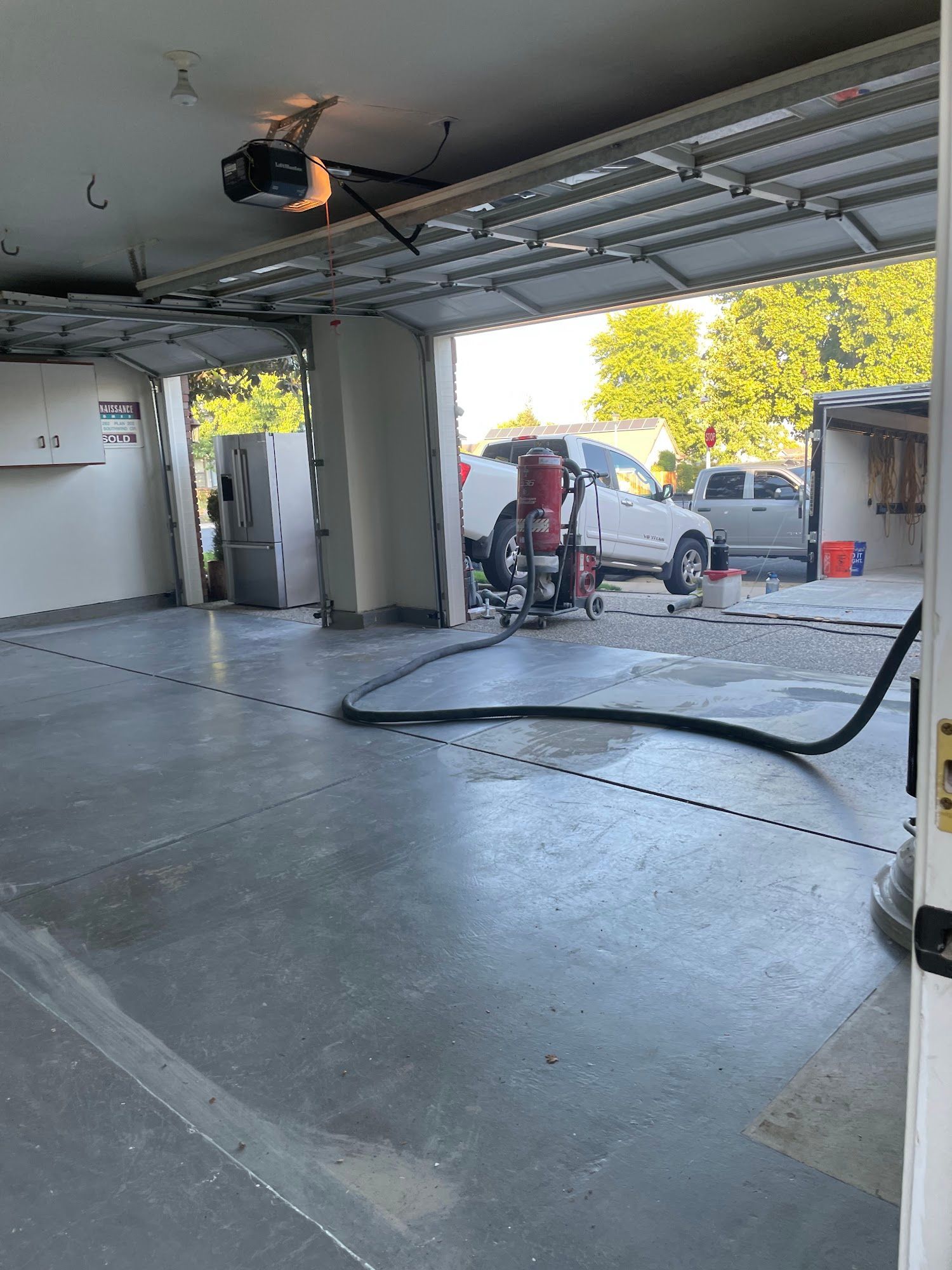 Garage interior with open door, vehicle, and equipment. Concrete floor.