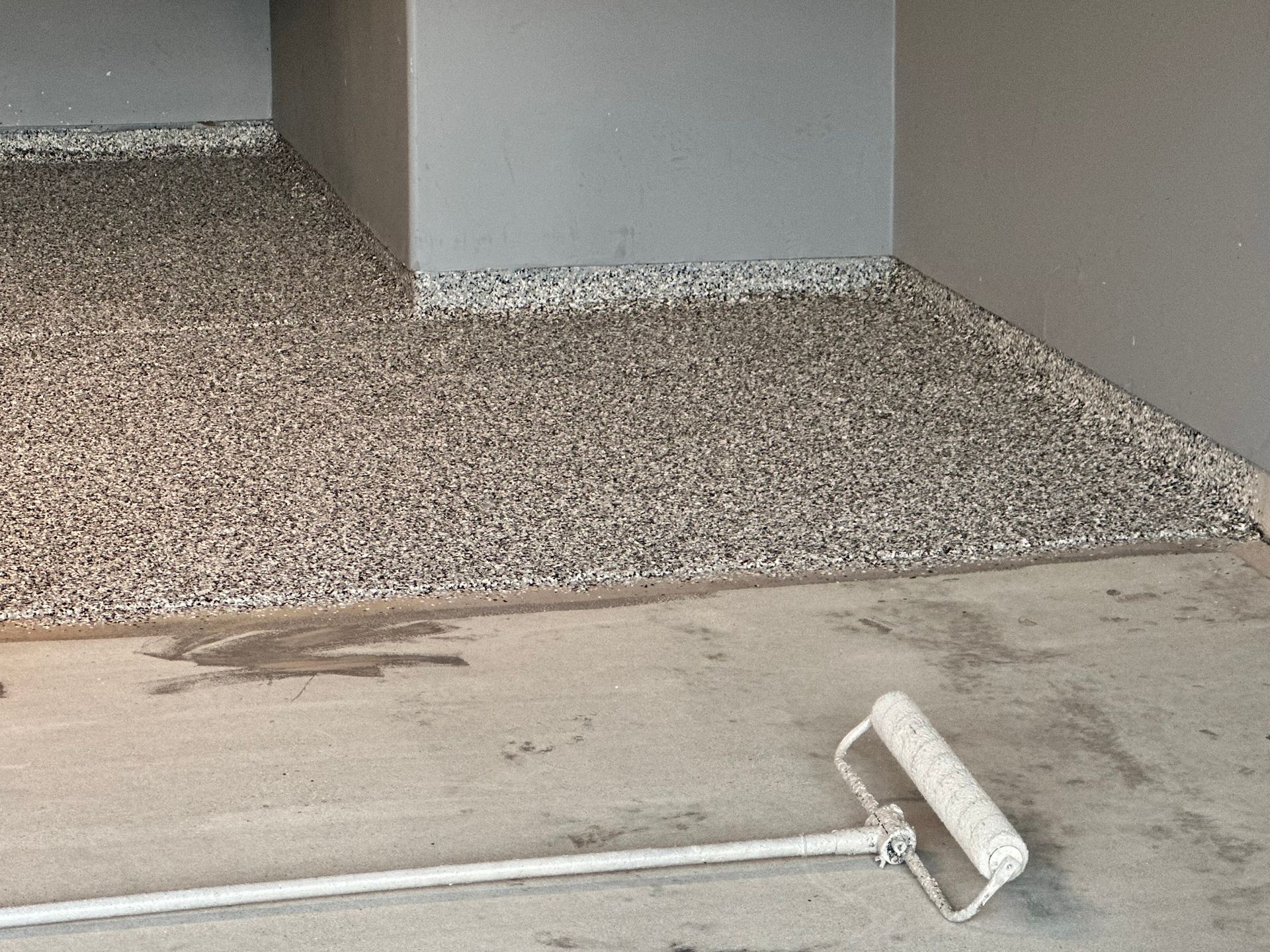 Epoxy-coated garage floor with speckled gray finish; roller in foreground.