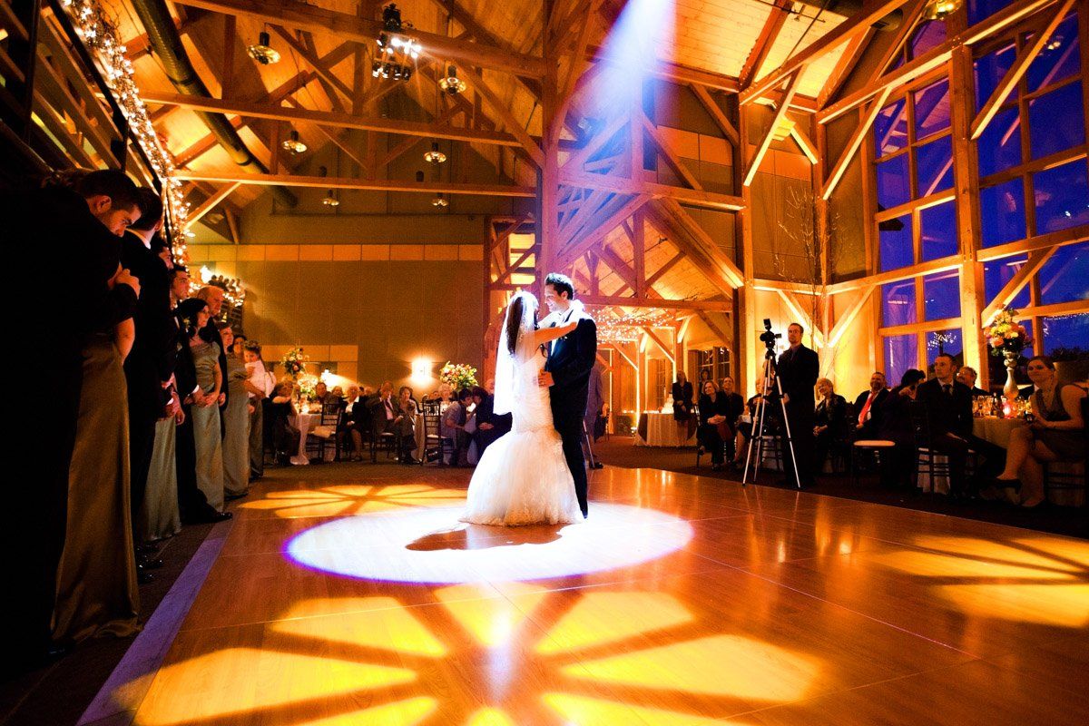 Bride and groom dance under a spotlight at wedding reception in a rustic venue.
