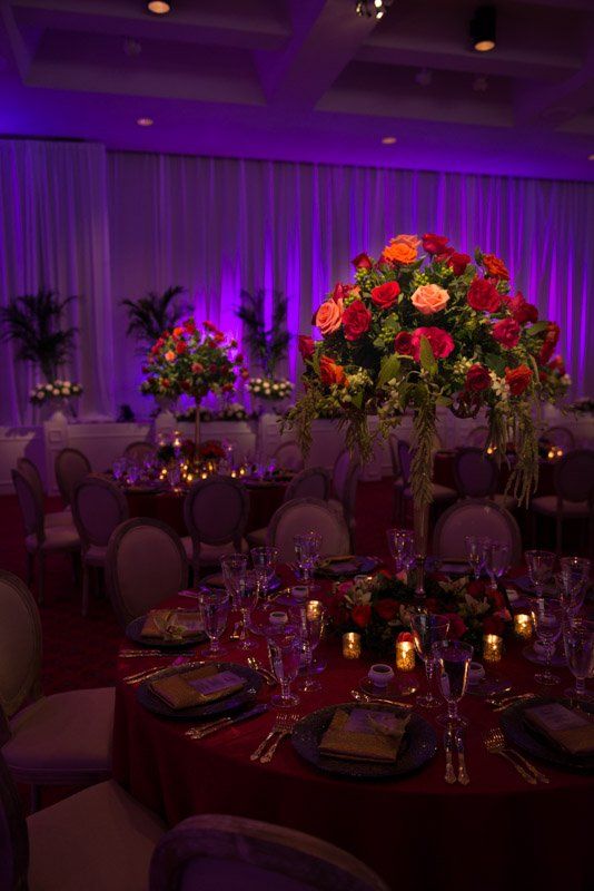 Elegant ballroom wedding with round tables, floral centerpieces, purple lighting.
