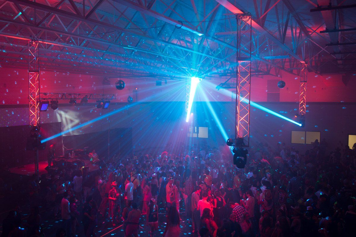 Dance party with blue and red laser lights over a crowd of people in a large room.