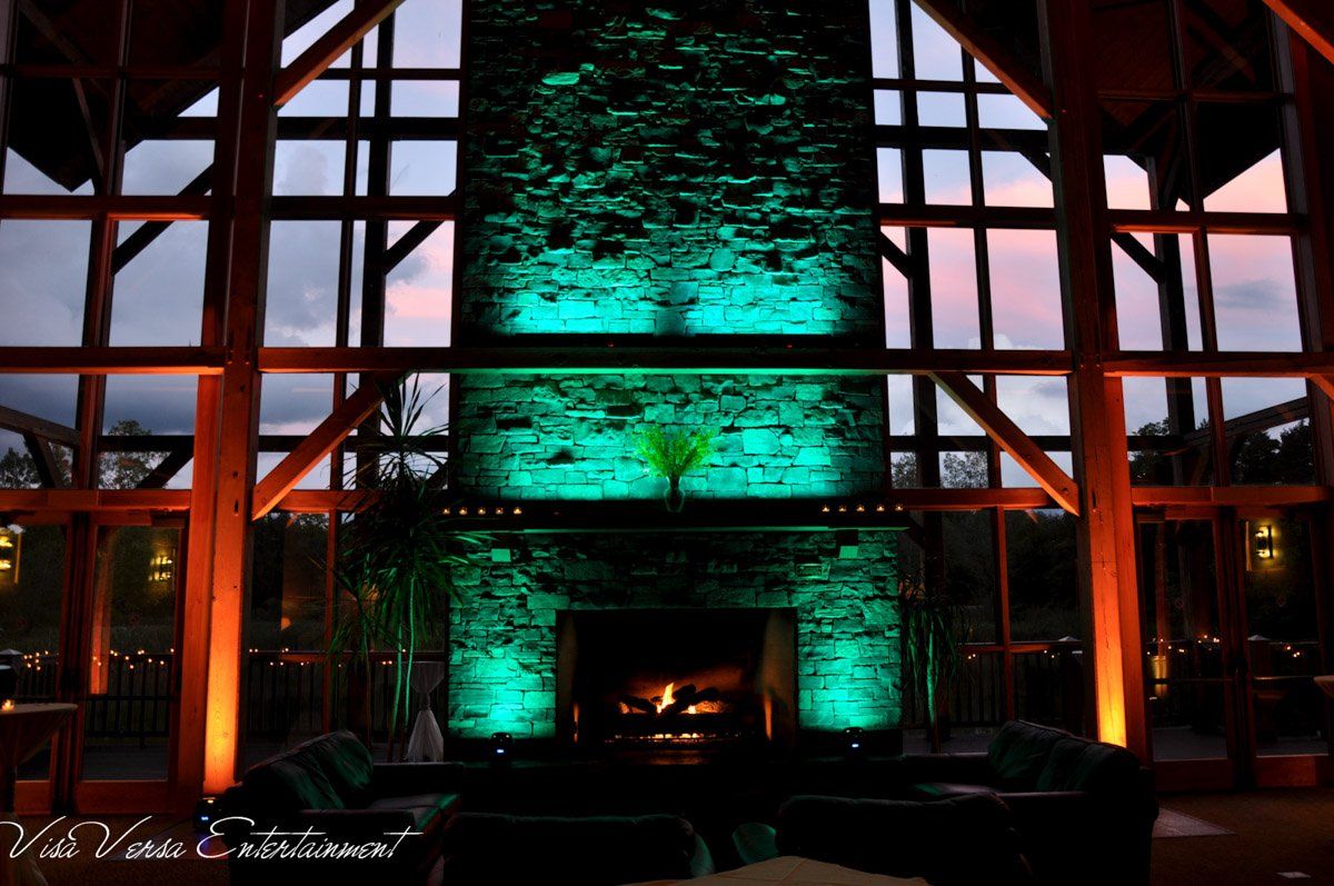 Large stone fireplace with green and orange lighting inside a building with large windows and a sunset view.