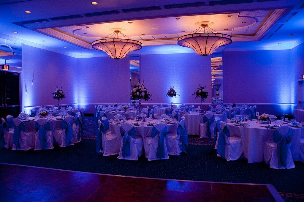 Banquet hall with round tables set for a celebration, bathed in blue light.