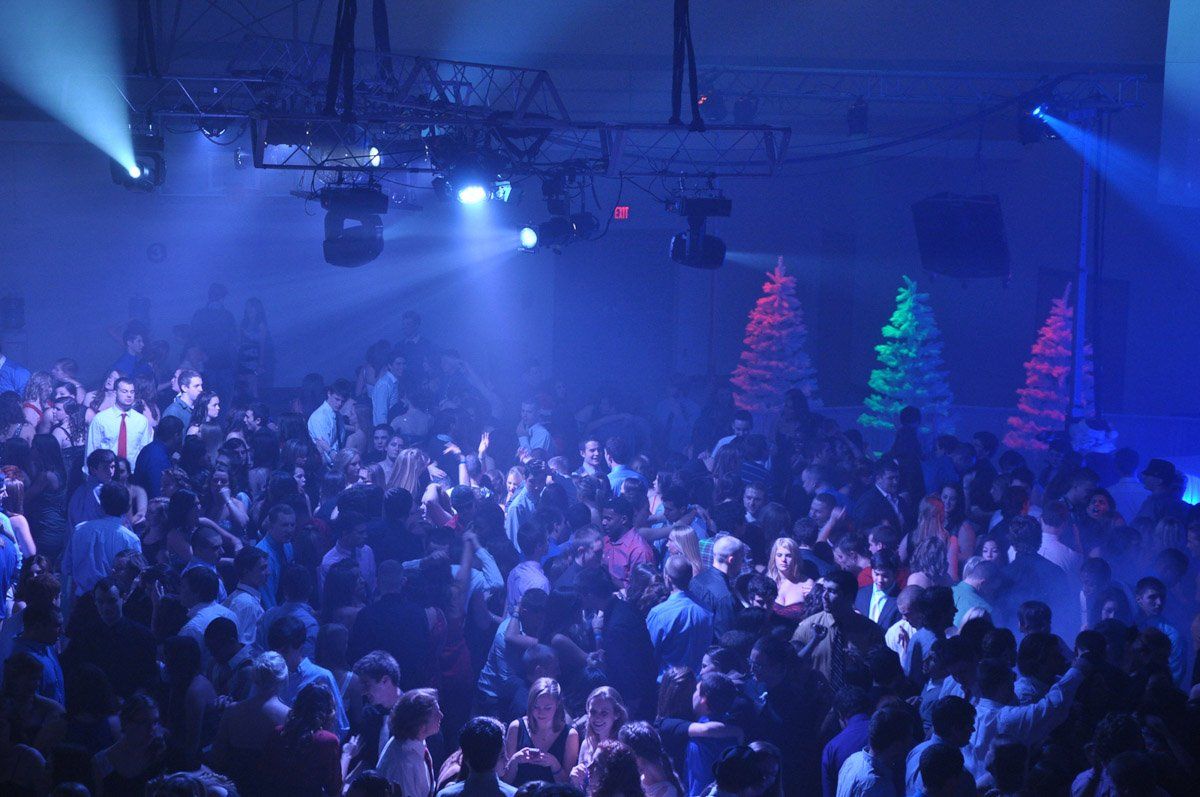 Party in a dark room with blue lighting, many people dancing. Christmas tree lights are visible.
