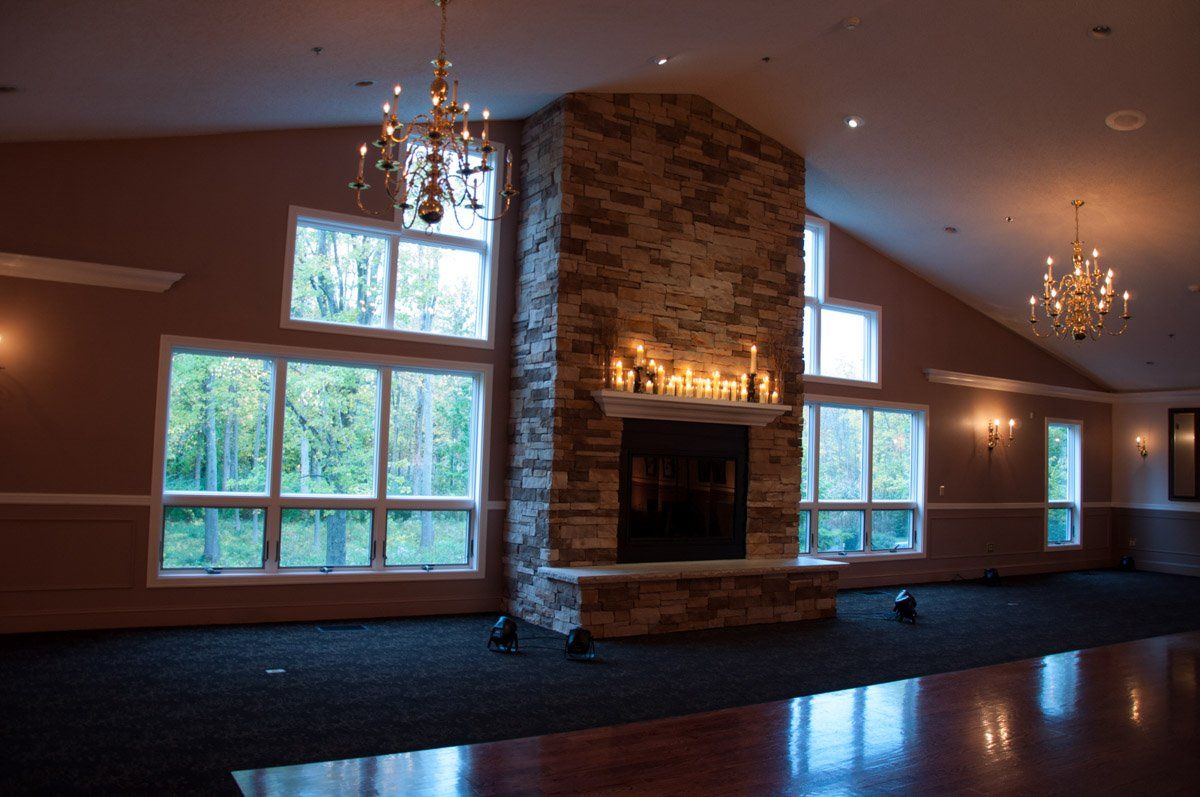 Large empty event space with a stone fireplace, windows, and chandeliers.