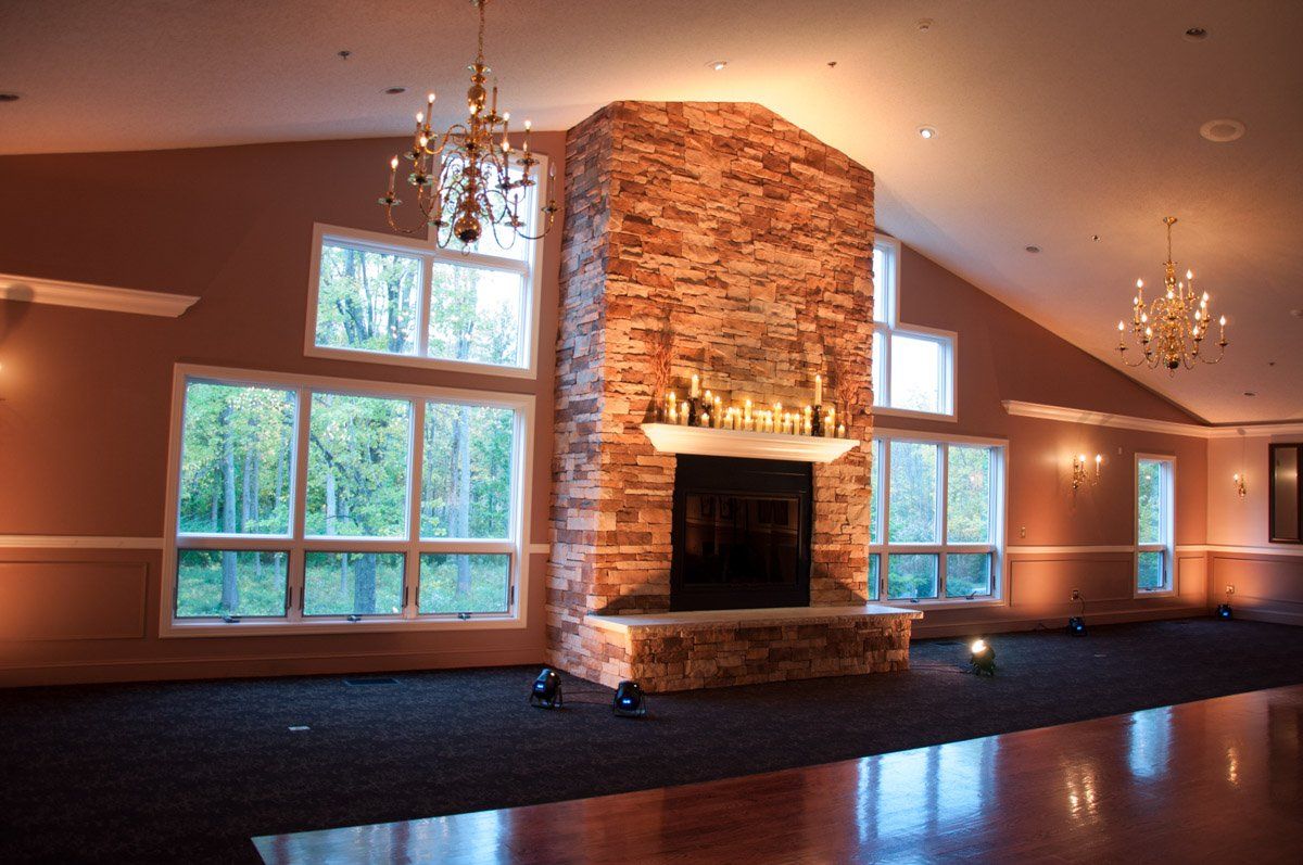A large room with a stone fireplace and windows overlooking a forest. Chandeliers hang from the ceiling.