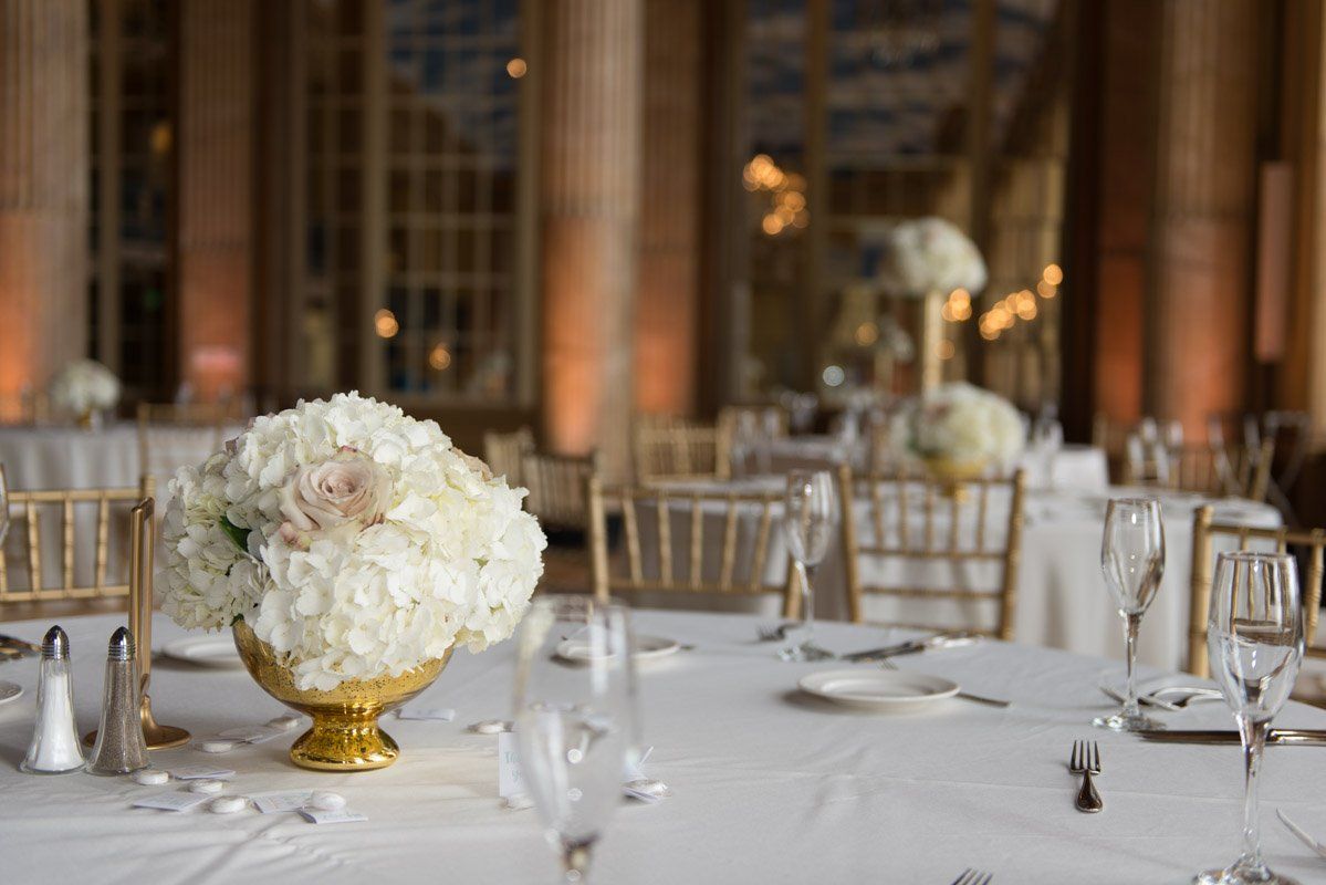 Wedding reception table with white floral centerpiece, gold accents, and champagne flutes in a warm, elegant setting.