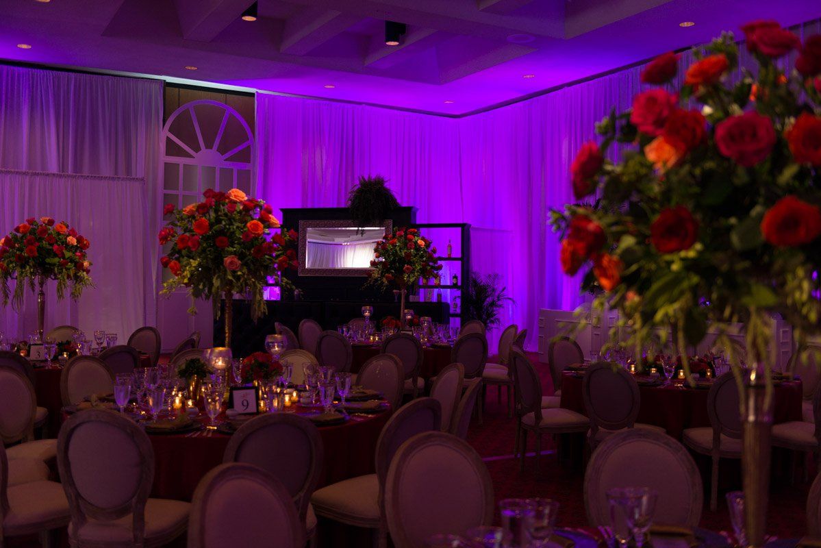 Elegant banquet hall with purple lighting, round tables set with flowers.