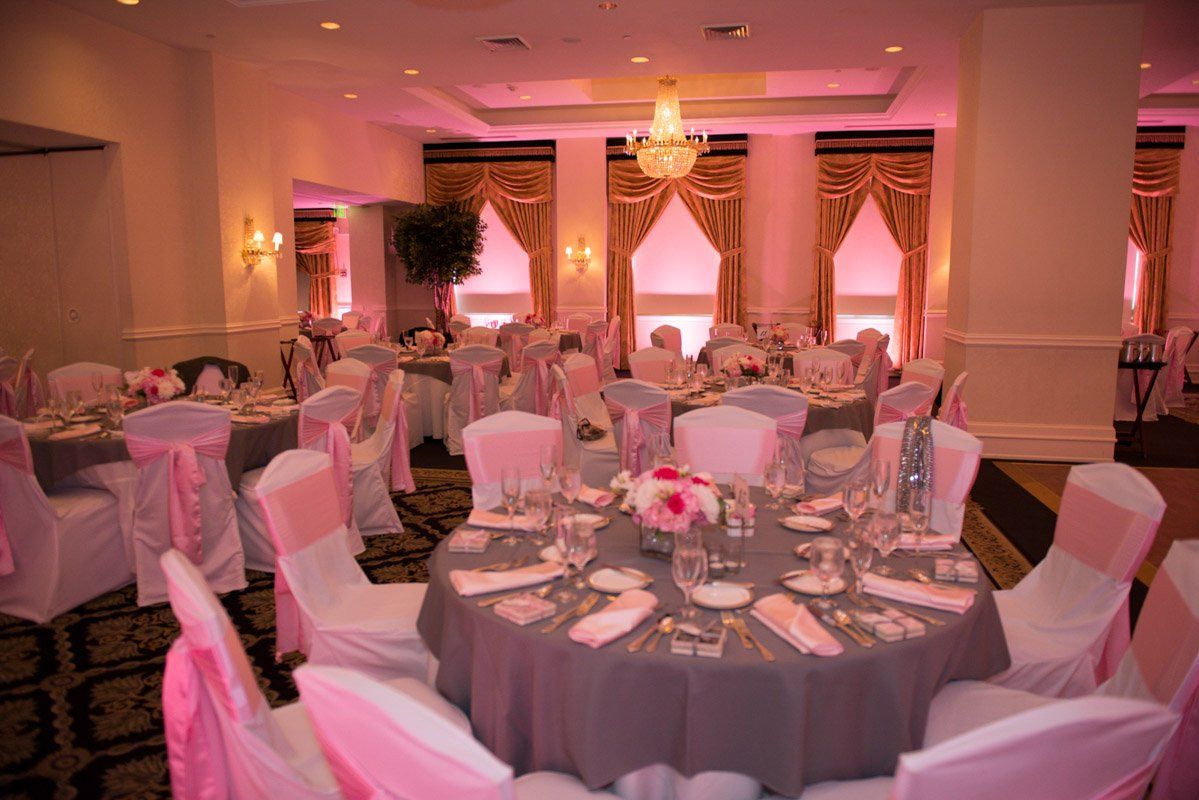 Formal dining room set for an event. Round tables with grey tablecloths and pink accents.
