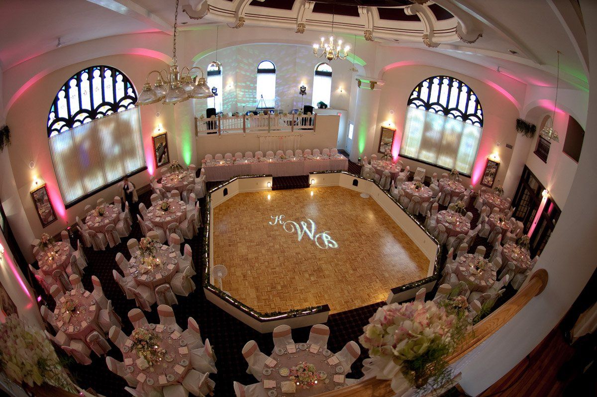 Wedding reception hall with tables, dance floor with initials, and lighting.