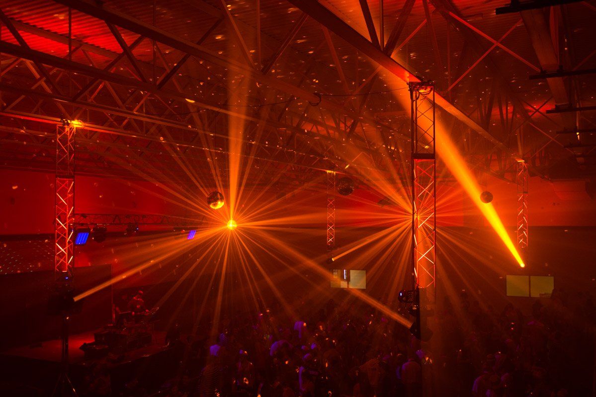 Orange and red laser lights illuminating a dark, crowded dance floor.