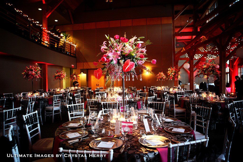 Elegant wedding reception with floral centerpieces, tables set, and red lighting.