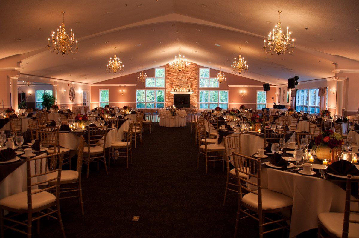 Elegant banquet hall with tables set for a formal event, gold chairs, chandeliers, and soft lighting.